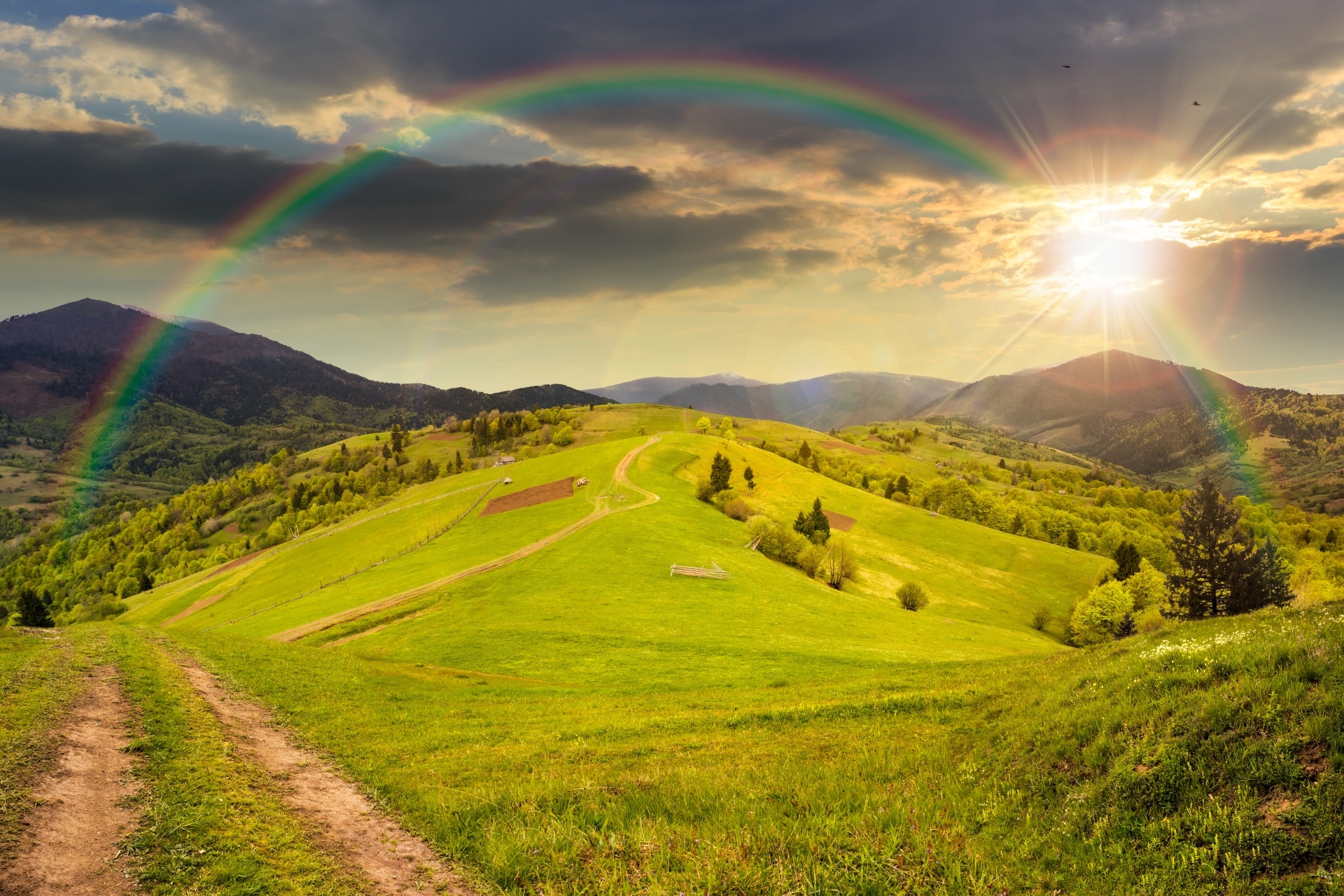 丘の上の牧草地と虹のかかる夕焼けの山々